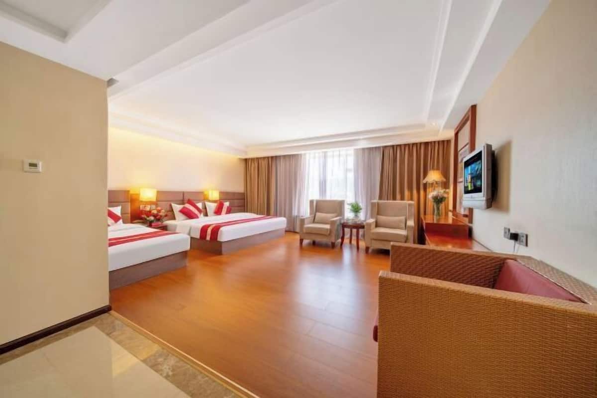 A hotel room with two beds, a sofa, a TV, and a window with curtains.