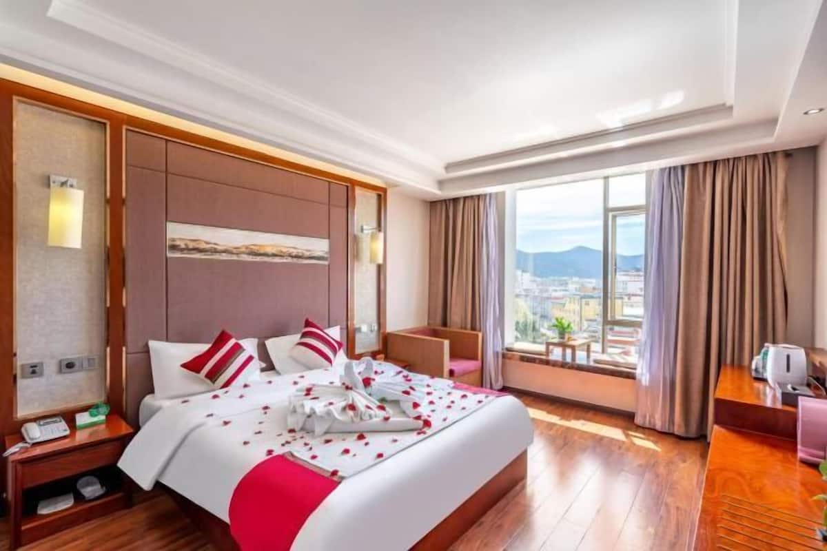 A hotel room with a large bed, a desk, a chair, and a view of the city.