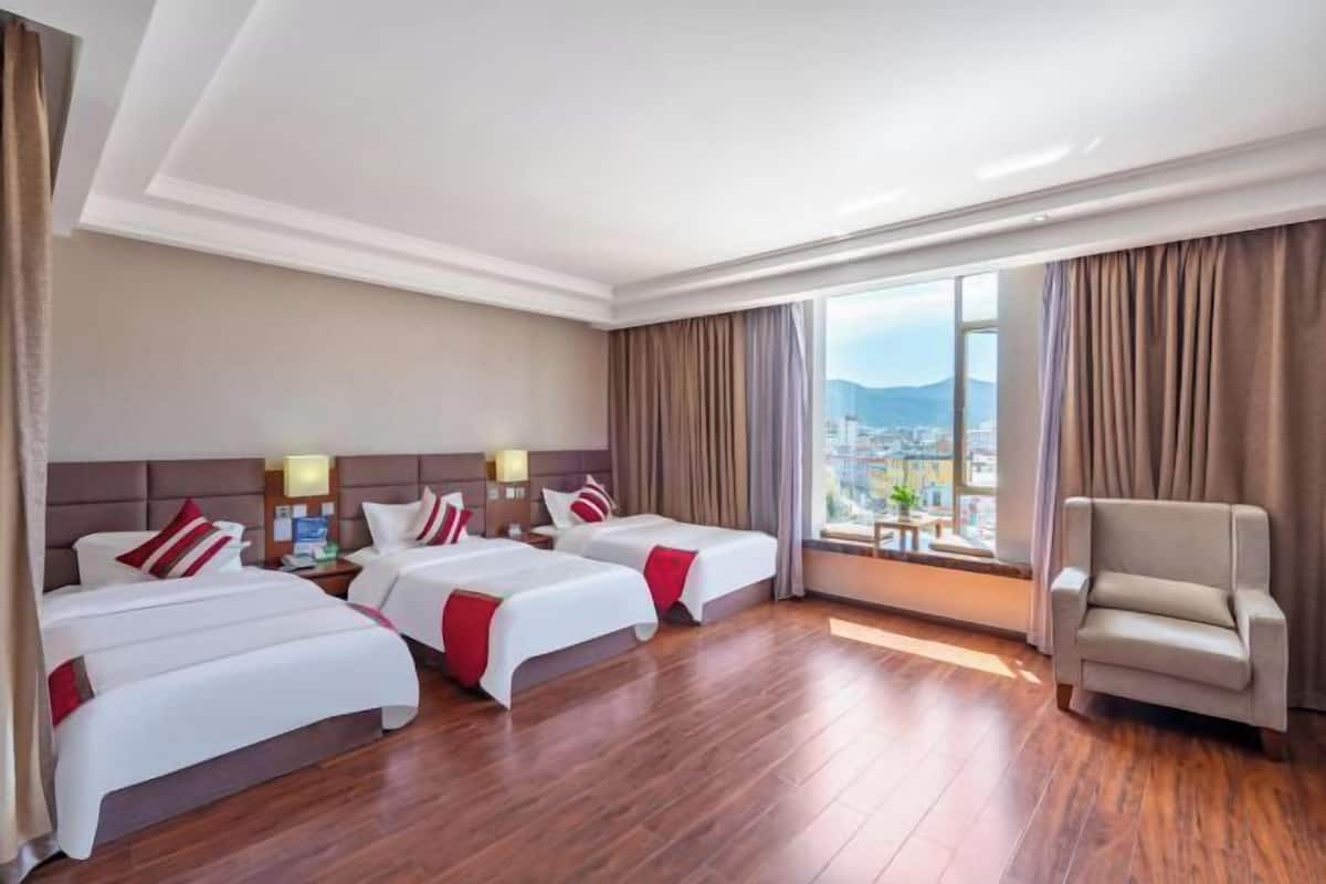 A hotel room with two beds, a chair, and a large window with a city view.