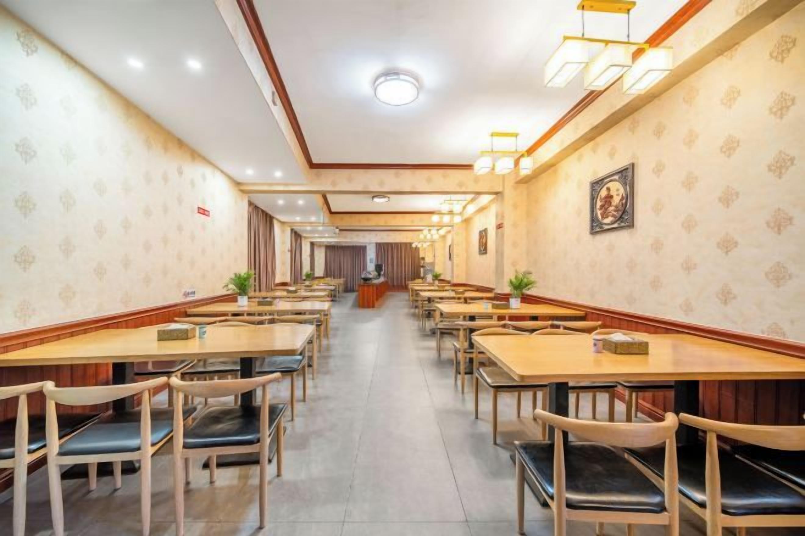 A hotel dining area with multiple tables and chairs, a reception desk, and patterned wallpaper.