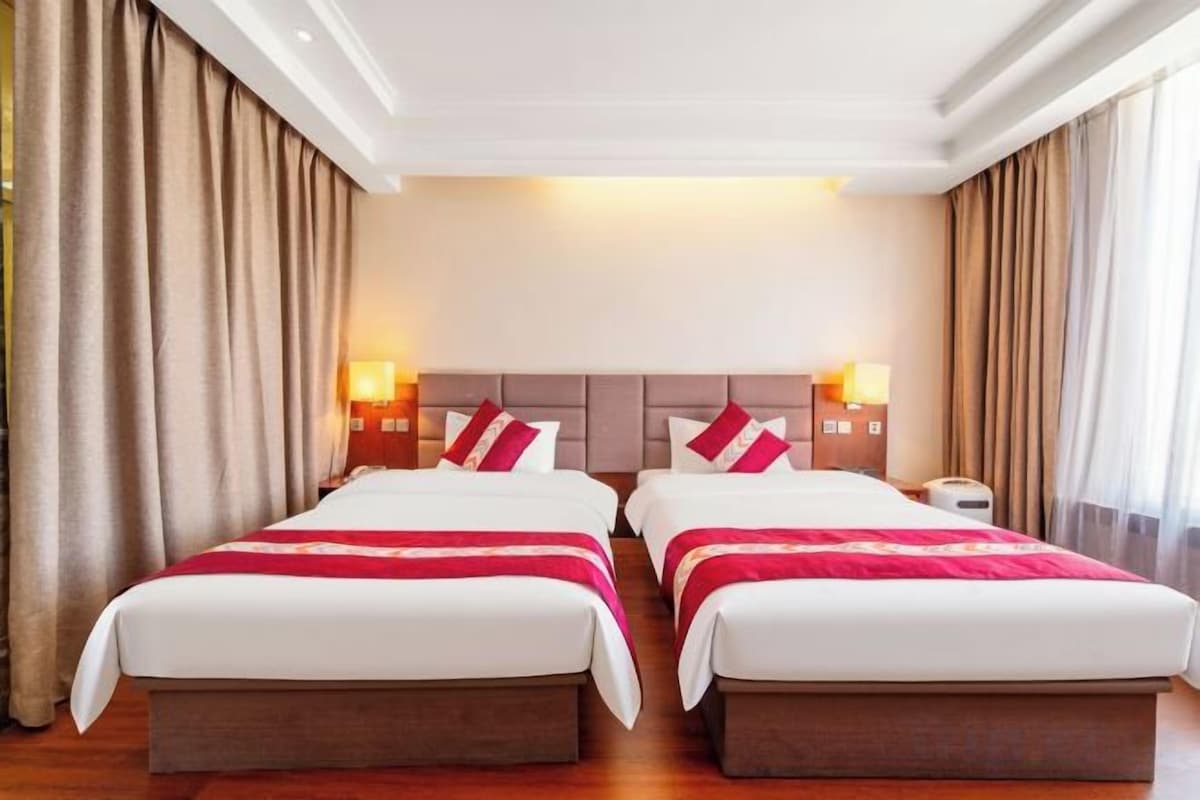 A hotel room with two beds, a nightstand, and a lamp.