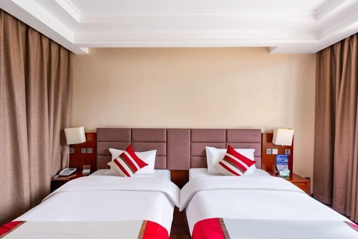 A hotel room with two beds, a headboard, bedside lamps, and curtains.