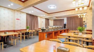 A hotel dining area with multiple tables and chairs, a buffet counter, and a large window with curtains.