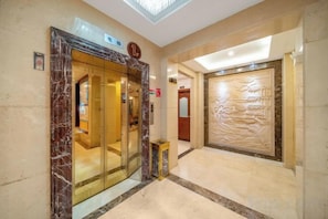 A hotel lobby with a marble entrance, a reception desk, and a decorative wall. - Salong Hotel (Shangri-La)