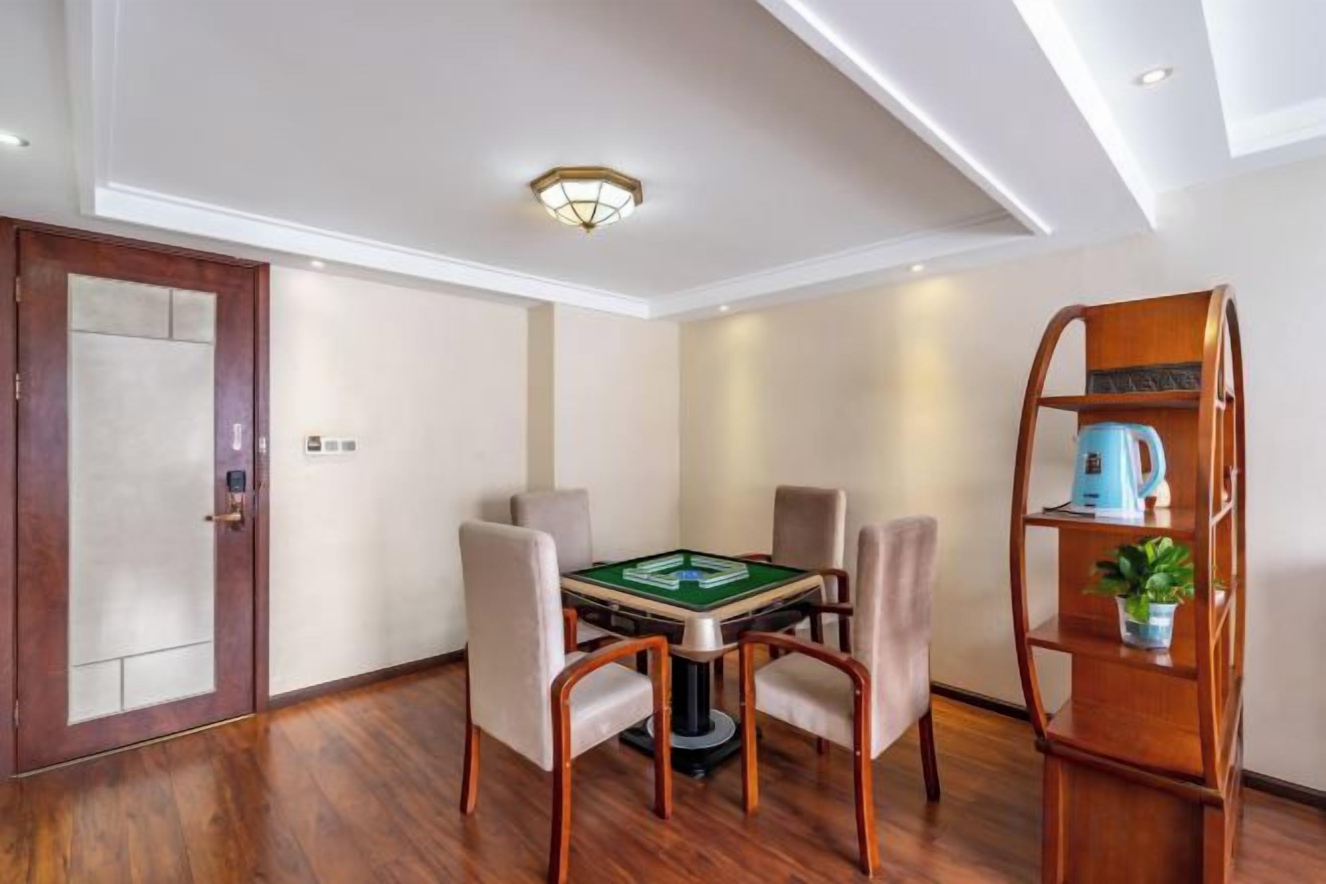 A room with a wooden floor, a green table with chairs, a bookshelf, and a door.