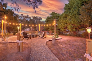 An outdoor seating area with a table and chairs, surrounded by a gravel path and string lights. - Steps to Oak Island Beach | Private Pool | Pet Friendly | Beach Gear (Oak Island)