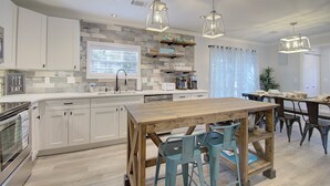 A modern kitchen with white cabinets, a wooden dining table, and teal chairs. - Steps to Oak Island Beach | Private Pool | Pet Friendly | Beach Gear (Oak Island)