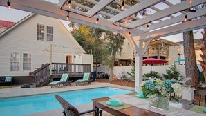 A backyard with a pool, outdoor seating, and a pergola with string lights. - Steps to Oak Island Beach | Private Pool | Pet Friendly | Beach Gear (Oak Island)