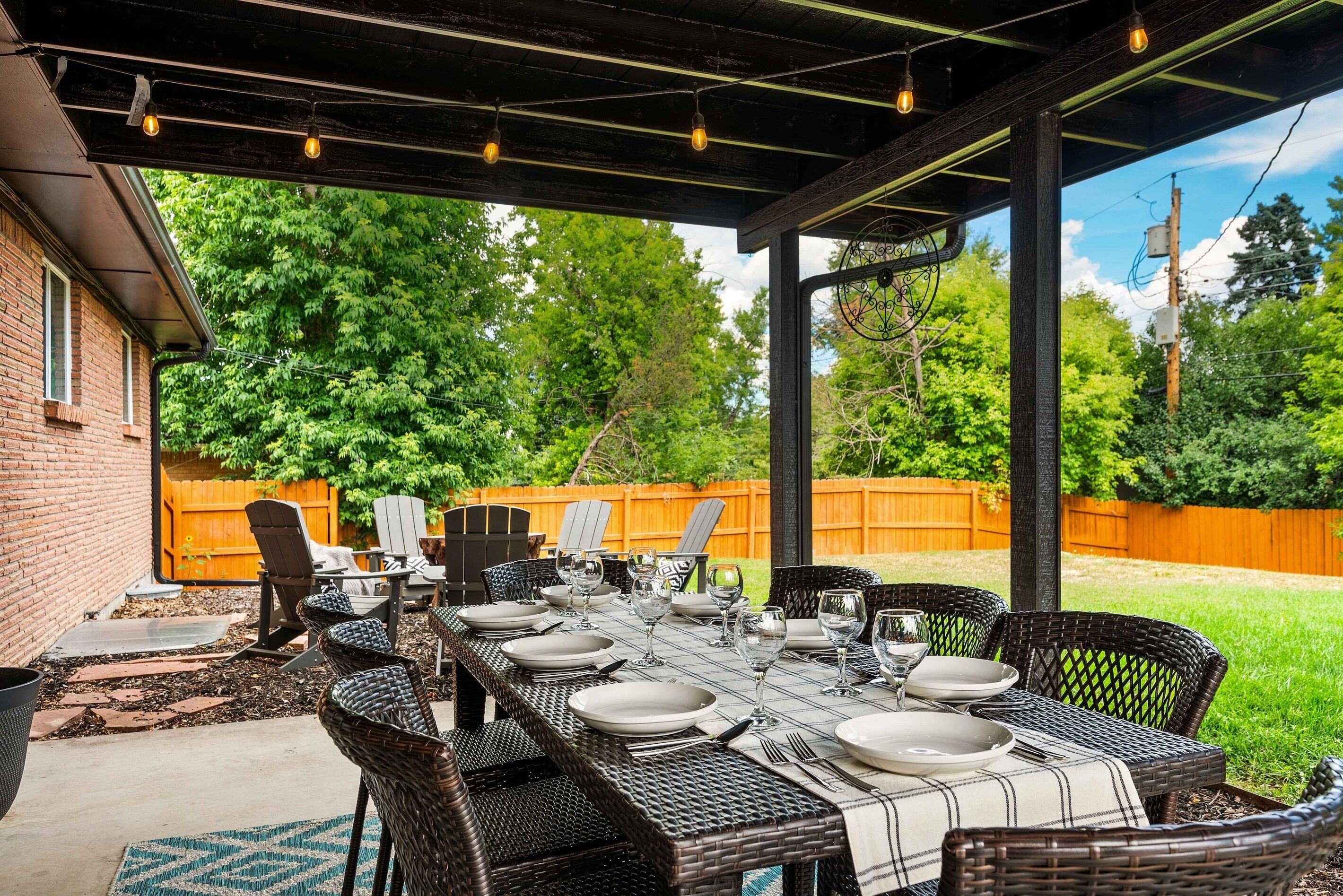 Covered patio with a large dining table, string lights, and comfy seating. Steps from the fire pit and fully fenced yard—perfect for meals, coffee, and relaxing outdoors.