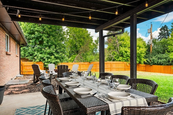 Covered patio with a large dining table, string lights, and comfy seating. Steps from the fire pit and fully fenced yard—perfect for meals, coffee, and relaxing outdoors.