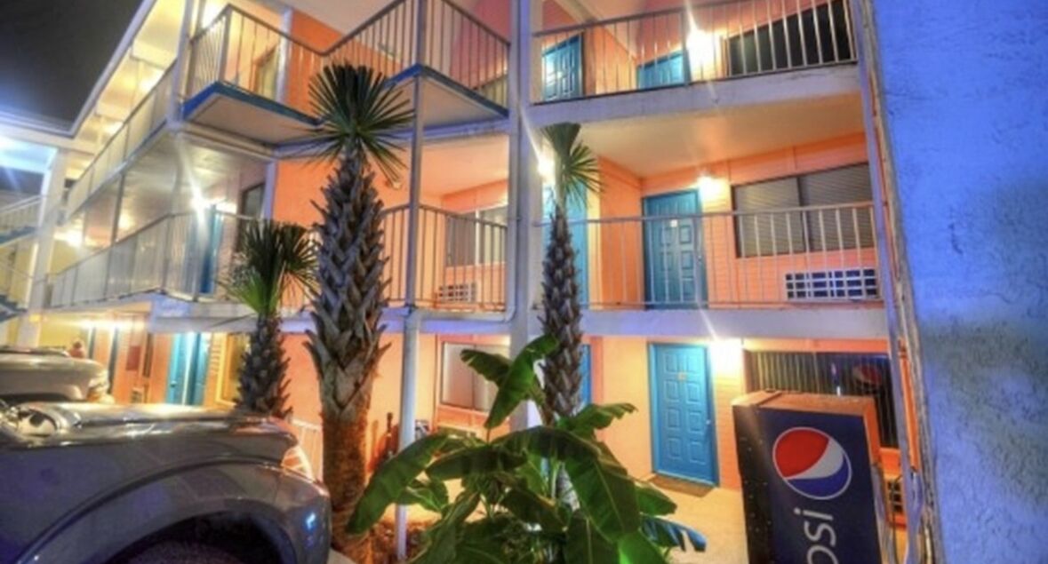 A multi-story hotel with balconies, palm trees, and a Pepsi vending machine.