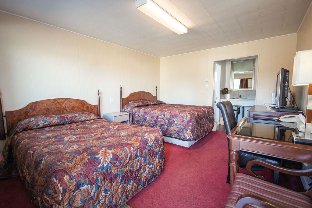 Hotellihuone, jossa on kaksi sänkyä, työpöytä, tuoli ja peili.