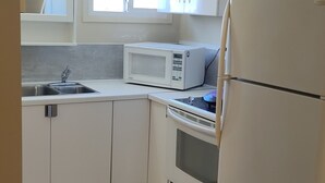 A compact kitchen with white cabinets, a microwave, a stove, and a refrigerator. - GOLDPAN MOTEL  (Quesnel)
