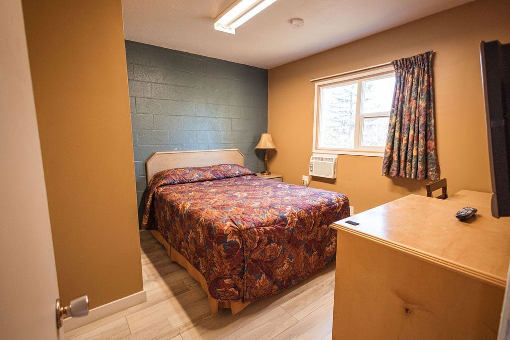 Une chambre à coucher avec un lit, une table de chevet, une lampe et une fenêtre avec des rideaux.