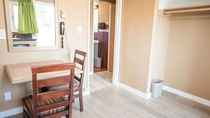 A room with a wooden dining table, two chairs, a mirror, a telephone, and a door leading to a bathroom. - GOLDPAN MOTEL  (Quesnel)