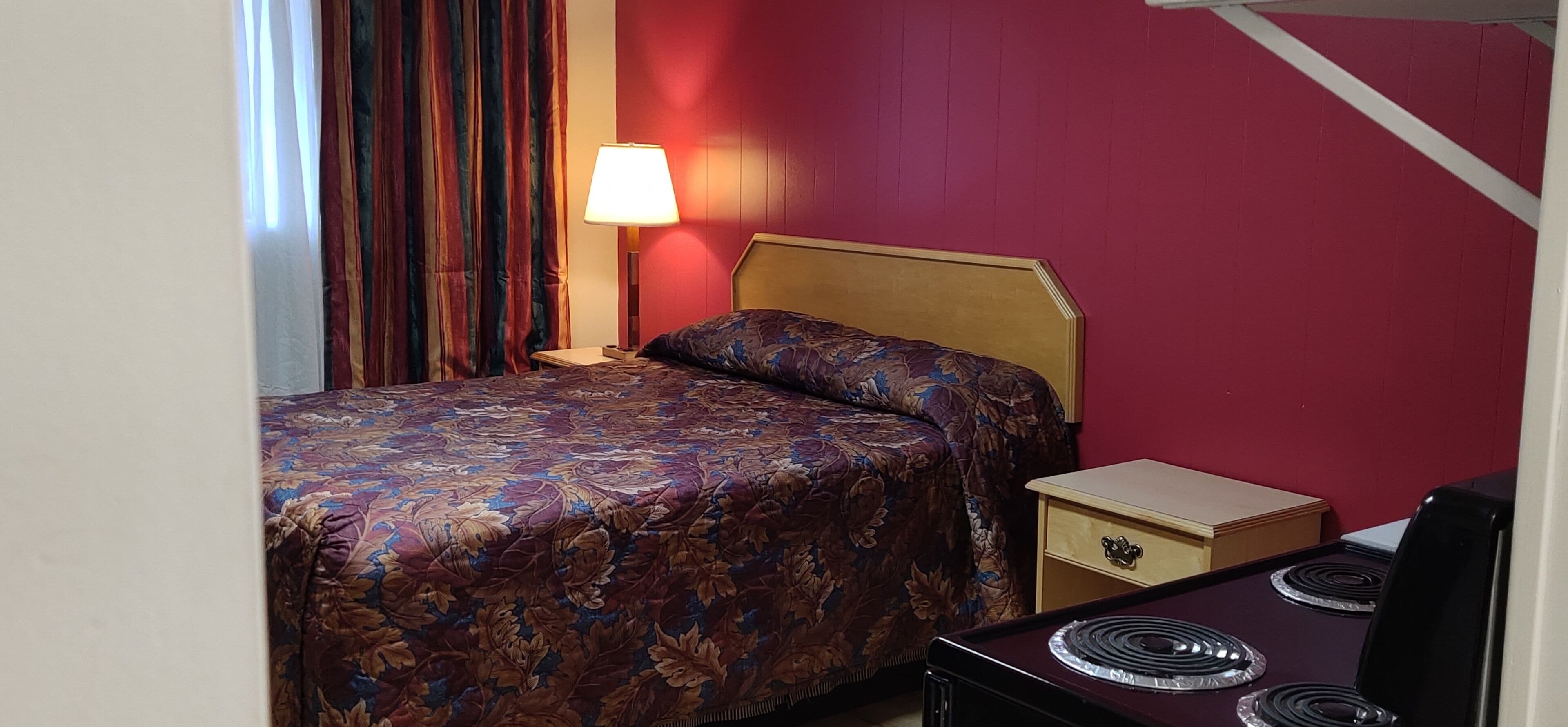 Ein Hotelzimmer mit Bett, Nachttisch, Lampe und kleinem Tisch mit Stuhl.