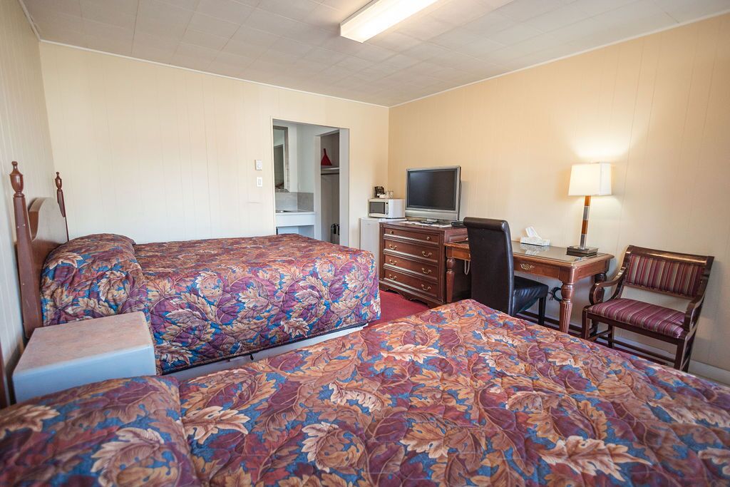 Une chambre d’hôtel avec deux lits, un bureau équipé d’un ordinateur, une chaise, une lampe et un four à micro-ondes.