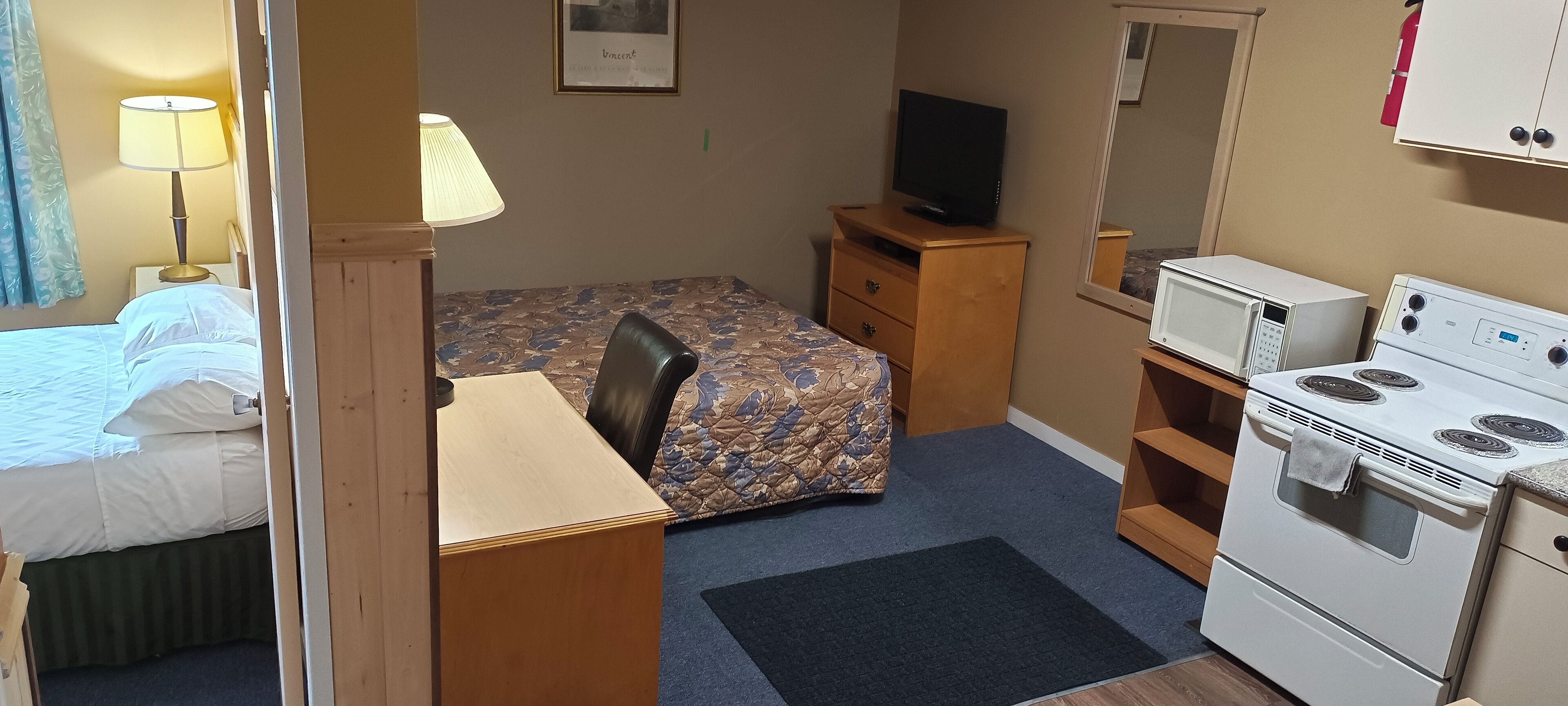 Une chambre d’hôtel de taille réduite, équipée d’un lit, d’un bureau, d’une chaise, d’une télévision, d’un four à micro-ondes et d’une cuisinière.
