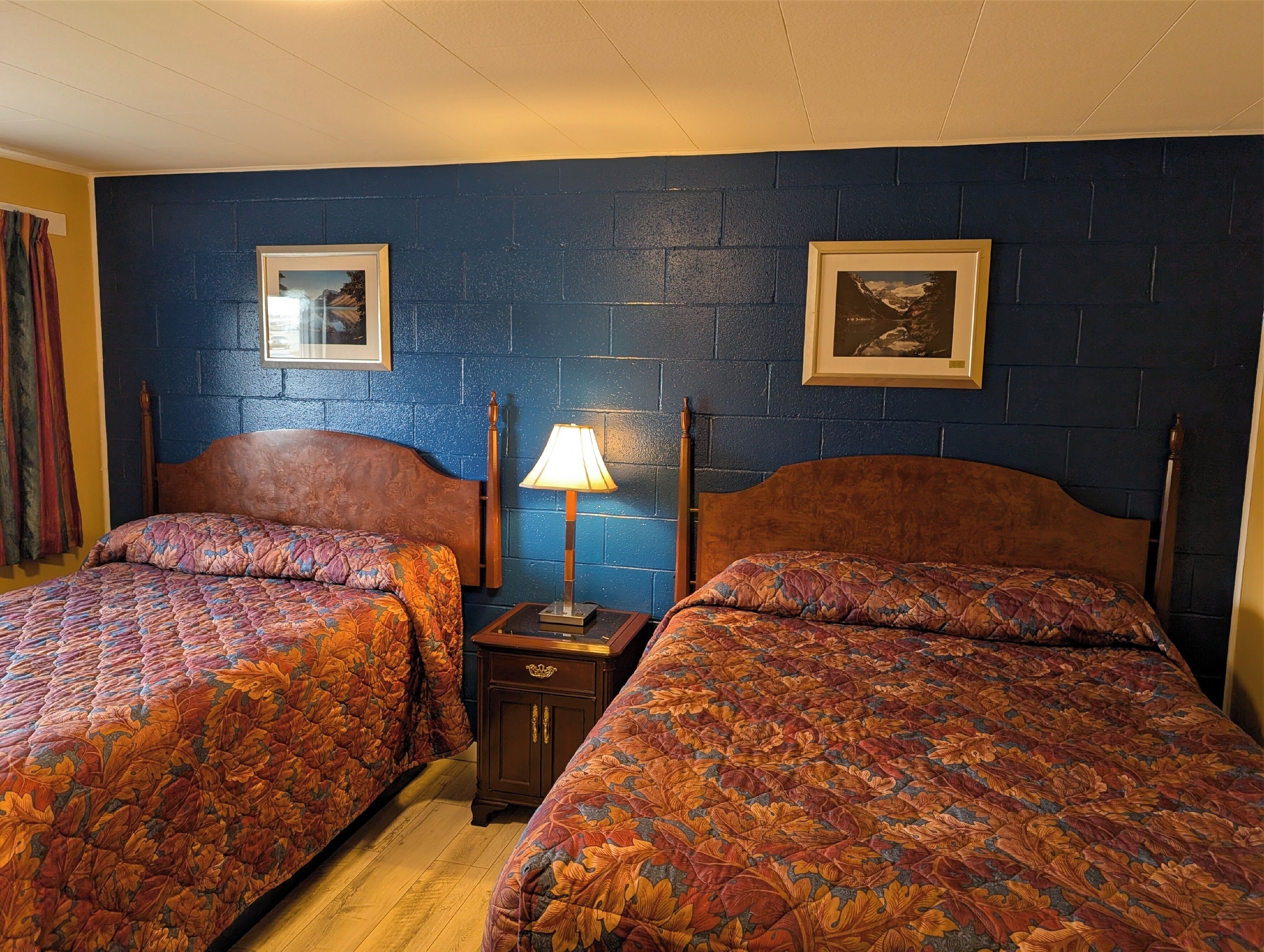 A room with two beds, a nightstand, a lamp, and two framed pictures on the wall.