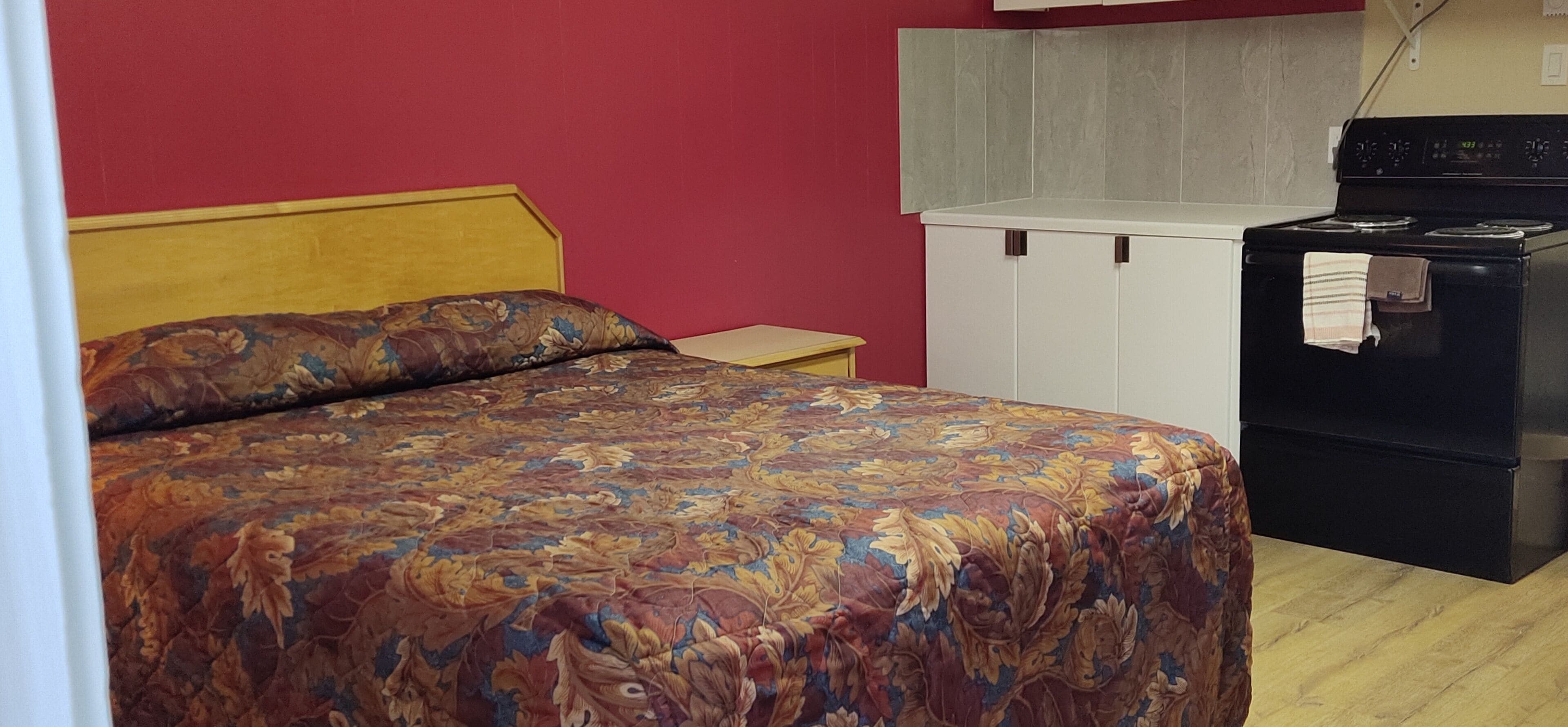 Ein Schlafzimmer mit einem Bett, einem Nachttisch, einem weißen Kleiderschrank und einem schwarzen Herd.