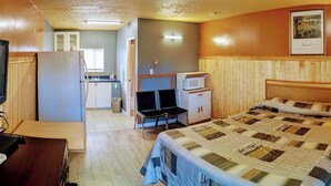 A compact hotel room with a bed, a television, a microwave, a small kitchenette, and a wooden headboard. - GOLDPAN MOTEL  (Quesnel)