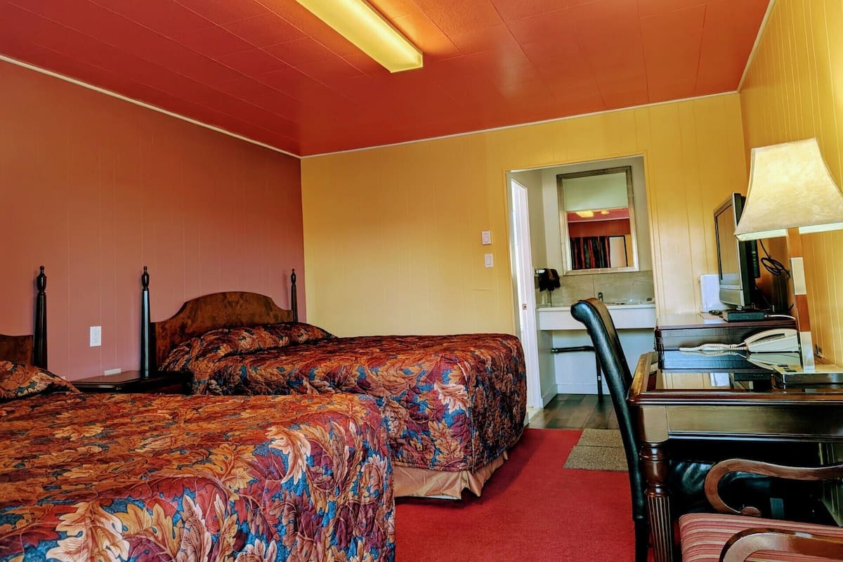 Habitación de hotel con dos camas, un escritorio, una silla y un baño visible a través de una puerta abierta.