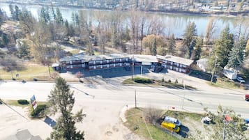 An aerial view of a building with a parking lot, surrounded by trees and a body of water.