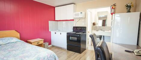 A compact room with a bed, kitchenette, and a chair.