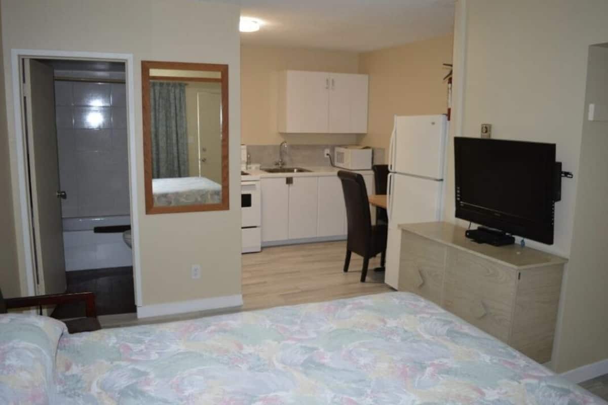Una habitación de hotel pequeña con cama, kitchenette, televisor y espejo.