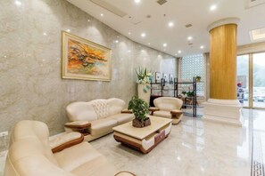 A modern hotel lobby with a marble wall, a large painting, a sofa set, a coffee table, and a decorative plant. - Kela Hotel (Fenyi)