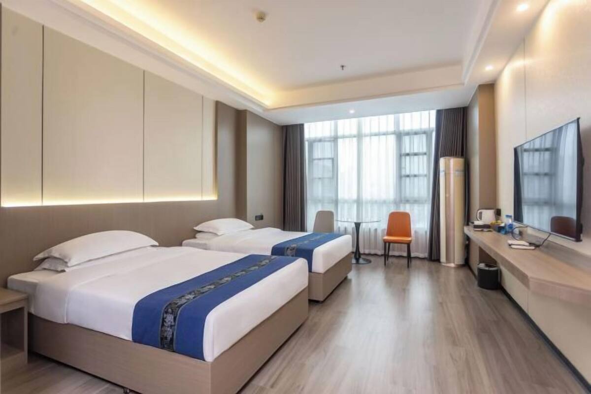 A hotel room with two beds, a desk, a chair, a TV, and a large window.