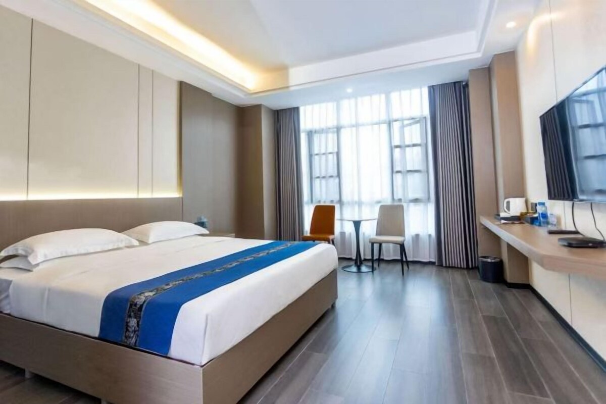 A hotel room with a large bed, a desk, a chair, and a TV.