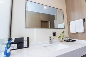 A modern bathroom with a large mirror, a white sink, and a black soap dispenser. - Kela Hotel (Fenyi)