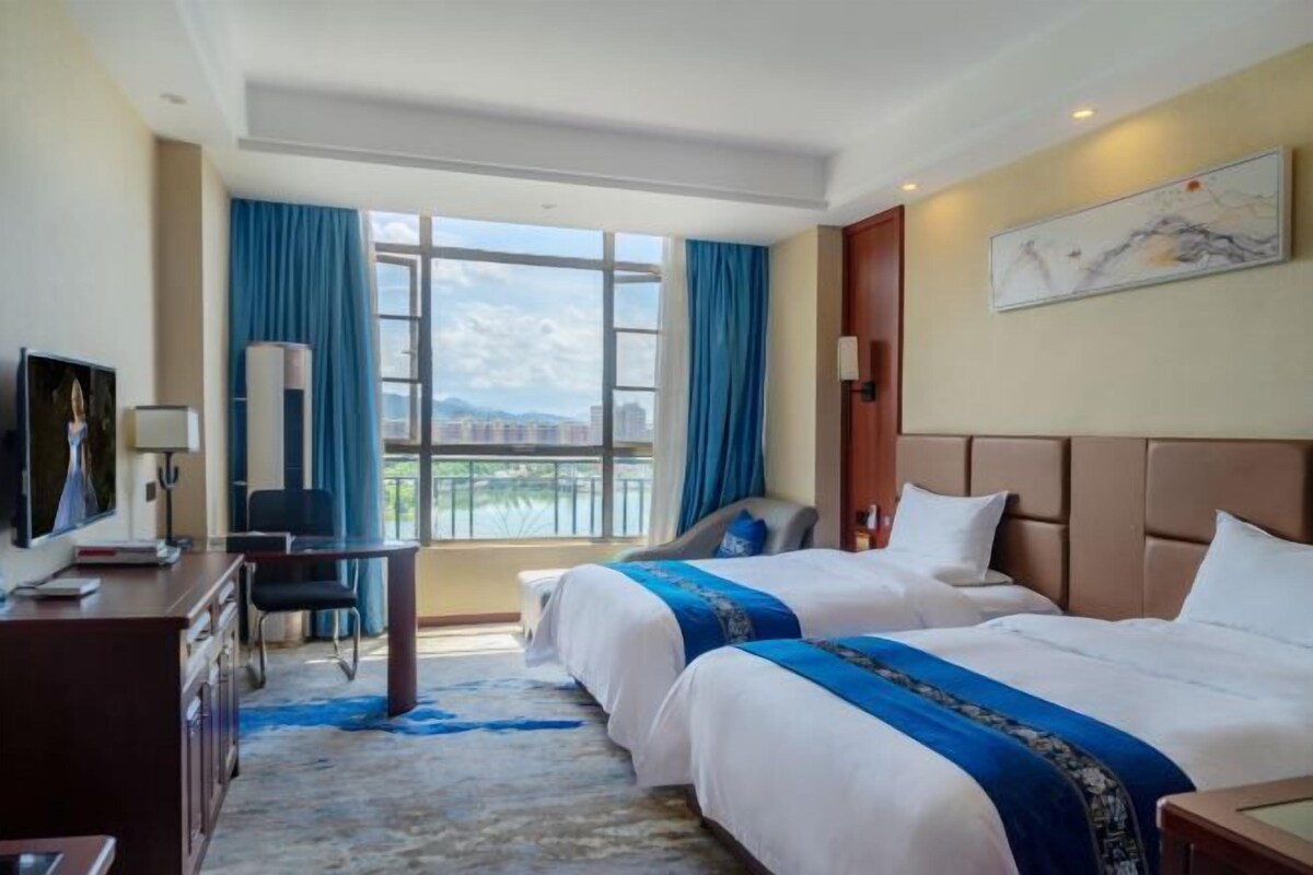 A hotel room with two beds, a desk, a chair, and a large window with a view.