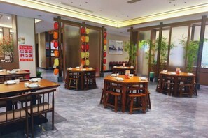 A restaurant with multiple tables and chairs, a tiled floor, and a view of the outdoors through large windows. - Kela Hotel (Fenyi)