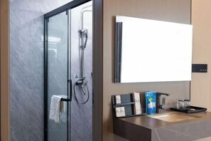 A modern bathroom with a glass shower enclosure, a large mirror, and a countertop with a soap dispenser and a tray. - Kela Hotel (Fenyi)