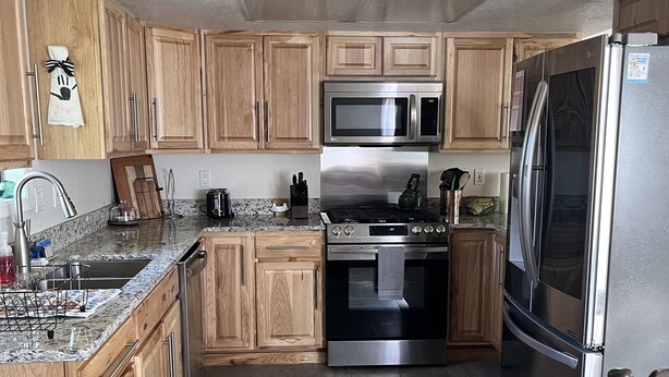 Eine moderne Küche mit Holzausstattung, Edelstahlgeräten, Granit Arbeitsplatten und einem schwarzen Teppich.