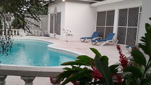 A swimming pool with lounge chairs, a white fence, and potted plants. - Villa Chinnor (Montego Bay)