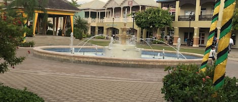 A courtyard with a central fountain, surrounded by buildings with balconies and a covered area.