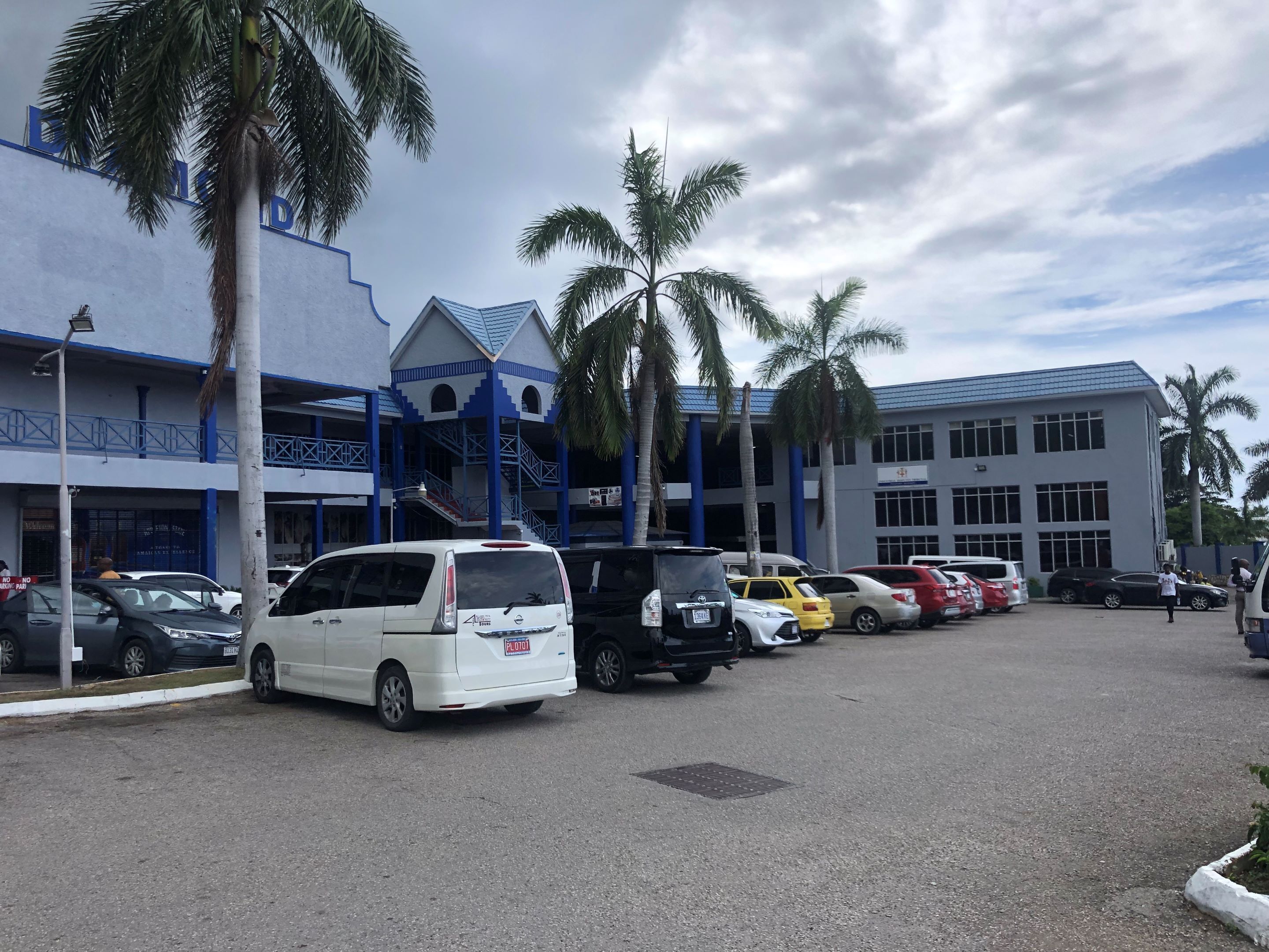 A parking lot with several cars, palm trees, and a building with blue and white exterior.