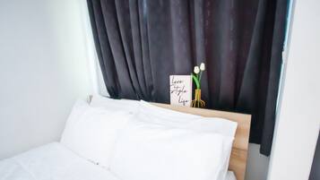 A neatly made bed with white linens, a dark curtain, and a sign with flowers and the words "Love Style Life".