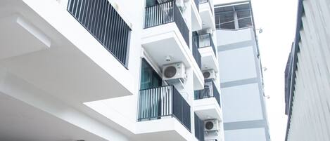 A modern multi-story building with balconies, large windows, and potted plants.