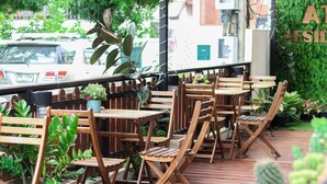 An outdoor seating area with wooden tables and chairs, surrounded by potted plants and a green wall. - ATC Residence (Bangkok)