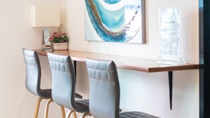 A modern dining area with a wooden table and three upholstered chairs with metal legs. A decorative painting is on the wall above the table. - ATC Residence (Bangkok)