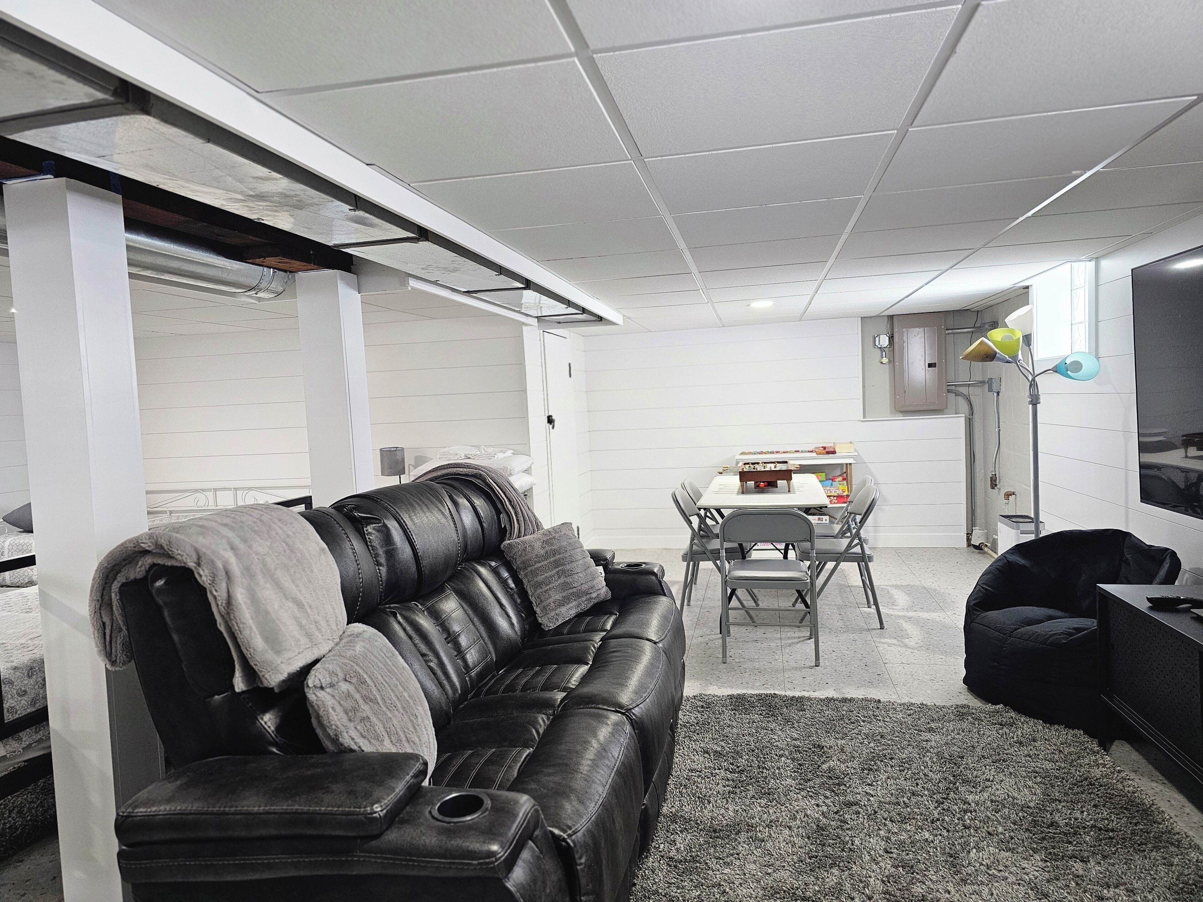 A modern living room with a black leather sofa, a dining table with chairs, and a small black ottoman.