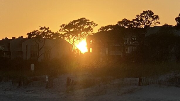 Solnedgang over et boligområde med huse og træer i silhuet mod himlen.