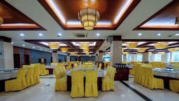 Un salón de banquetes con mesas redondas y sillas amarillas, vigas de techo de madera e iluminación empotrada.