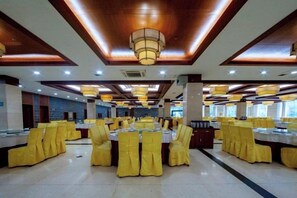 A banquet hall with round tables and yellow chairs, wooden ceiling beams, and recessed lighting. - Tianlongshan Hotel (Dexing)