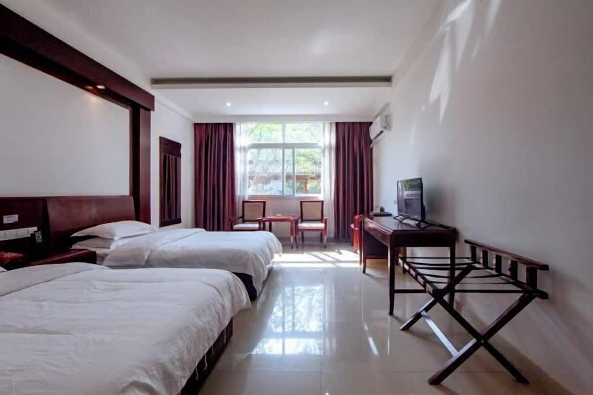 A hotel room with two beds, a desk with a chair, a TV, and a window with curtains.