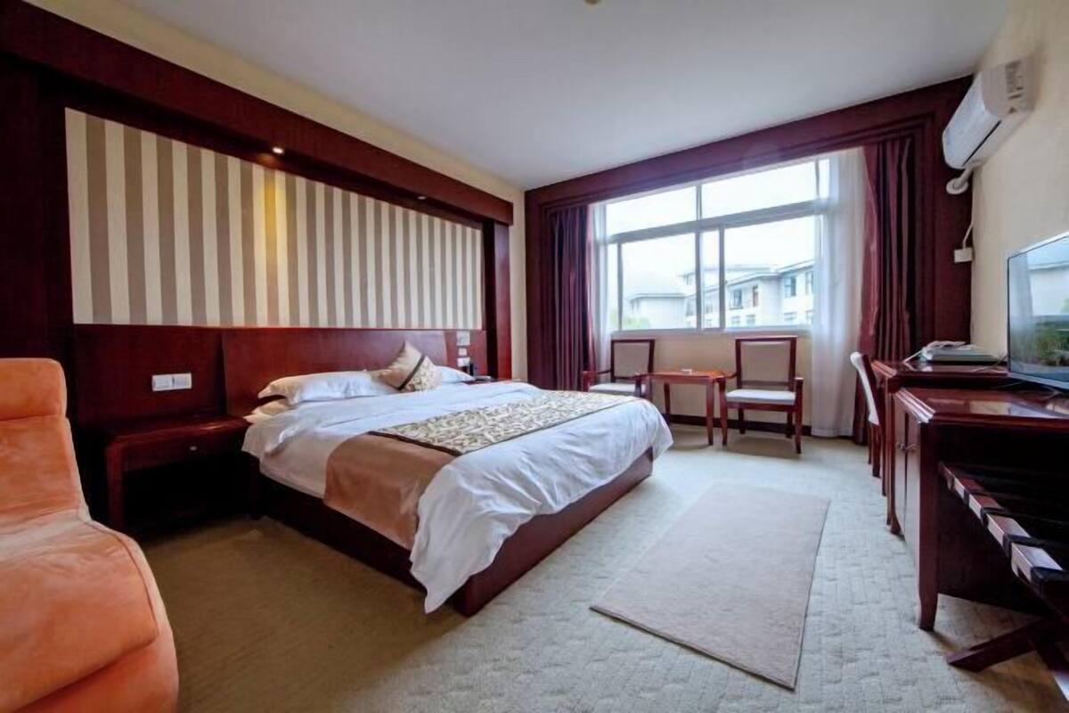 A hotel room with a large bed, a desk with a chair, a television, and a window with curtains.